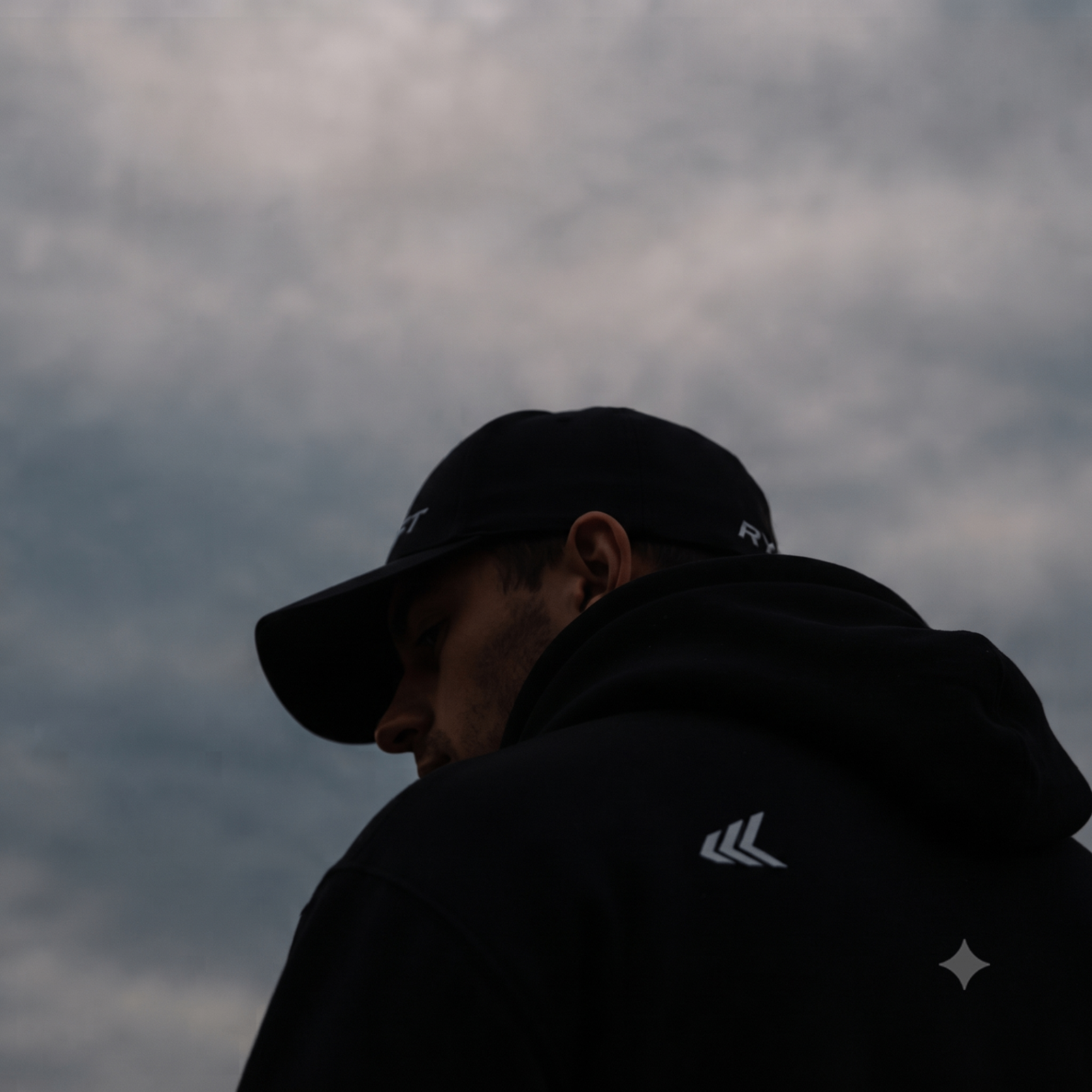 Close portrait in RYFT hoodie and cap under a moody sky