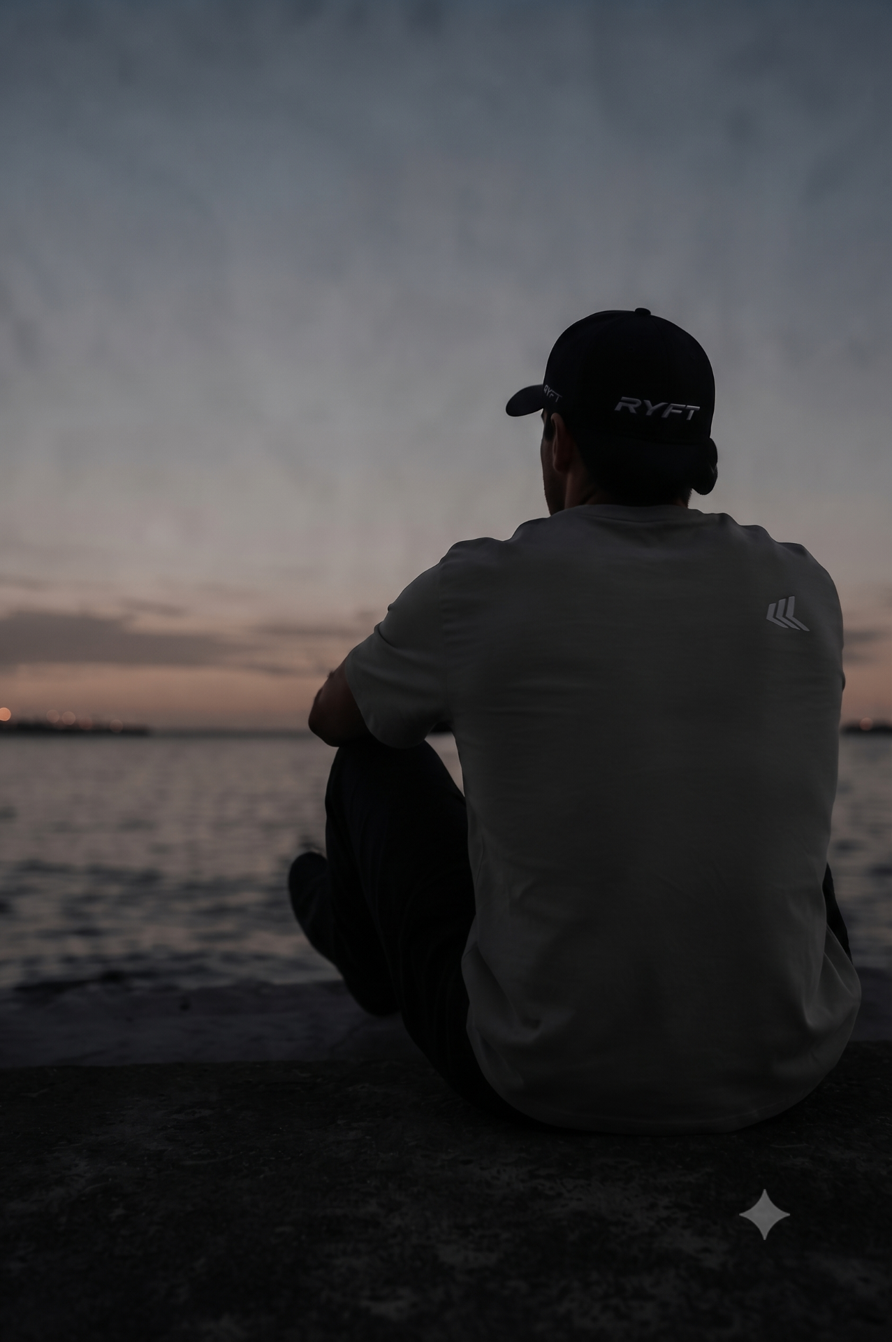 Figure in RYFT tee and cap at dusk by the water